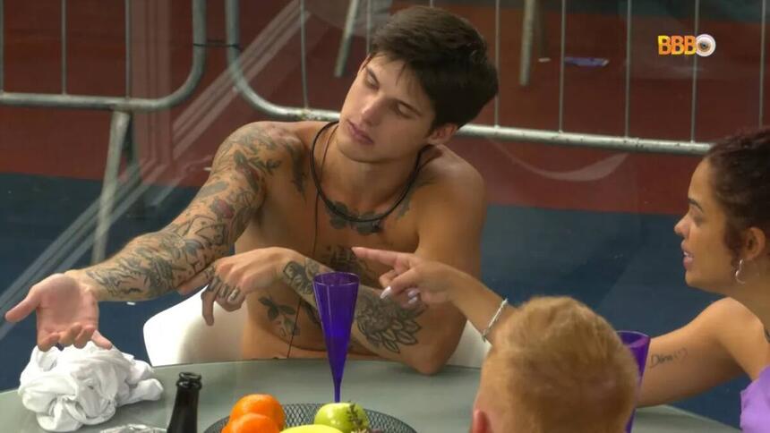 Paula apontando para o braço de Gabriel, que mostra suas tatuagens.
