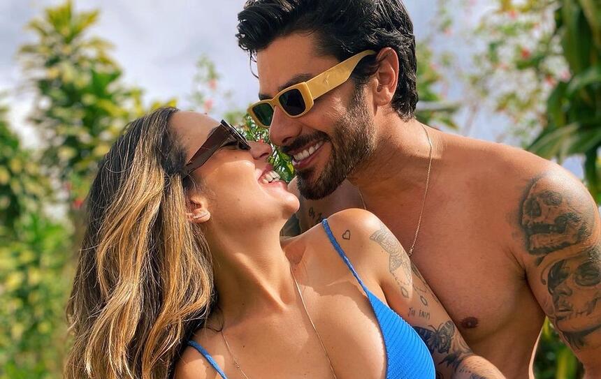 Renan Oliveira com óculos de sol, sorrindo, sem camisa, abraçado com a namorada de biquini azul e óculos de sol