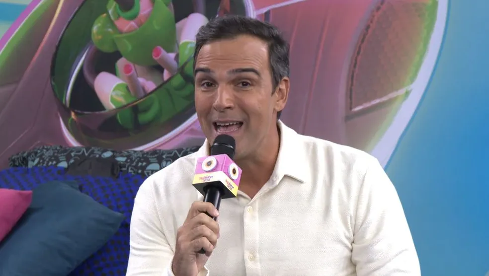 Tadeu Schmidt de camisa branca e calça dentro da Casa de Vidro, apresentando o espaço em chamada