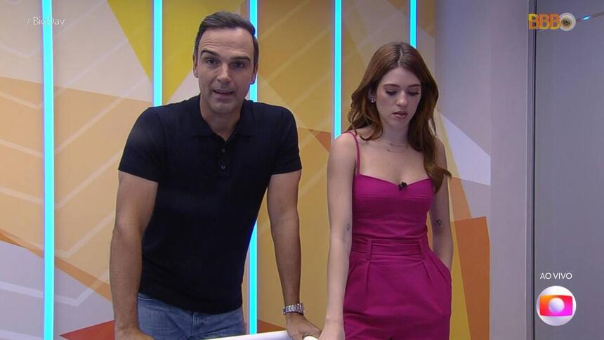 Tadeu Schmidt, de camiseta polo preta e calça jeans, e Ana Clara, com um vestido rosa, direto da casa do BBB 23, durante trecho da divulgação dos nomes ao vivo