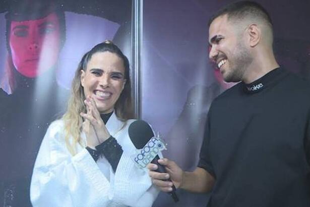 Wanessa Camargo vestindo roupa branca e preta sorrindo em entrevista ao Fofocalizando. Ao lado está o repórter do programa também sorriso e vestindo uma camisa preta.