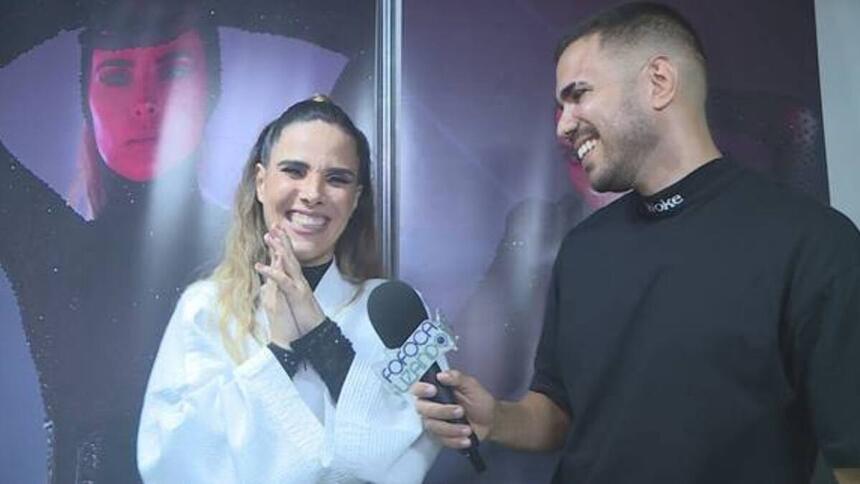 Wanessa Camargo vestindo roupa branca e preta sorrindo em entrevista ao Fofocalizando. Ao lado está o repórter do programa também sorriso e vestindo uma camisa preta.