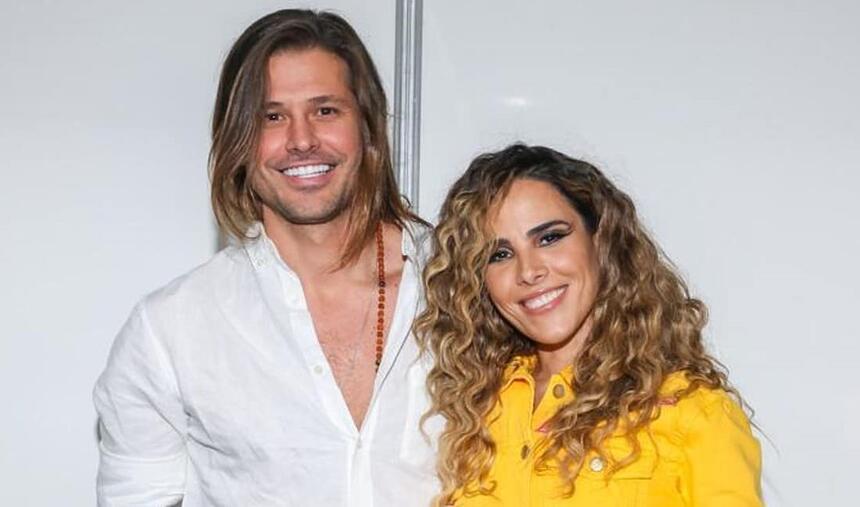 Wanessa Camargo de cabelo cacheado, sorrindo, de camisa social amarela, ao lado de Dado Dolabella, que está de camisa social branca, sorrindo, de cabelo liso e solto