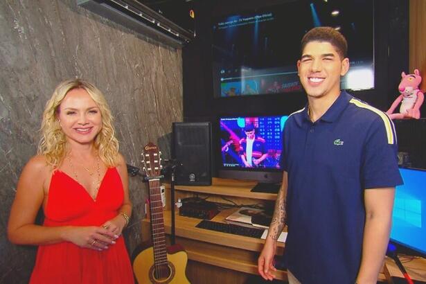 Eliana sorrindo vestindo um vestido vermelho ao lado de Zé do Vaqueiro que também sorri e veste uma camisa polo azul. Ambos estão em um estúdio de gravação de música.