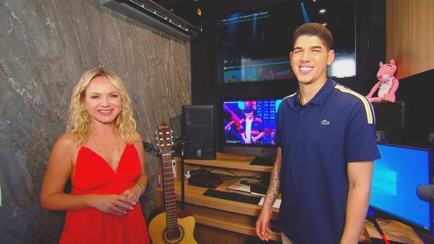 Eliana sorrindo vestindo um vestido vermelho ao lado de Zé do Vaqueiro que também sorri e veste uma camisa polo azul. Ambos estão em um estúdio de gravação de música.