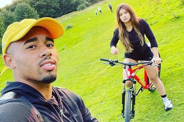 Raiane Lima e Gabriel Jesus em foto posada juntos. Ela está em cima de uma bicicleta