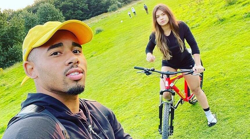 Raiane Lima e Gabriel Jesus em foto posada juntos. Ela está em cima de uma bicicleta