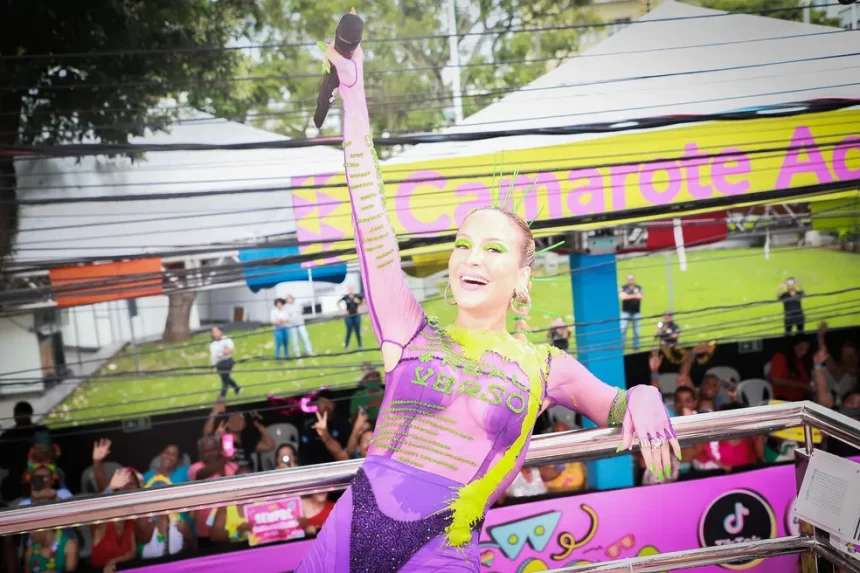 Claudia Leitte sorrindo, em pé, com as mãos pra cima durante percurso no carnaval de salvador