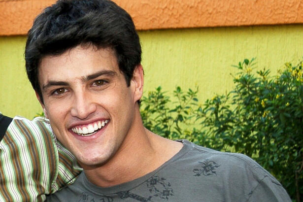 Alexandre Slaviero de camisa cinza, sorrindo, durante gravação de Malhação, da TV Globo