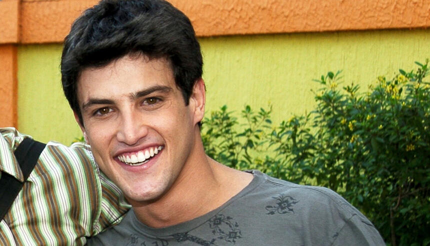 Alexandre Slaviero de camisa cinza, sorrindo, durante gravação de Malhação, da TV Globo