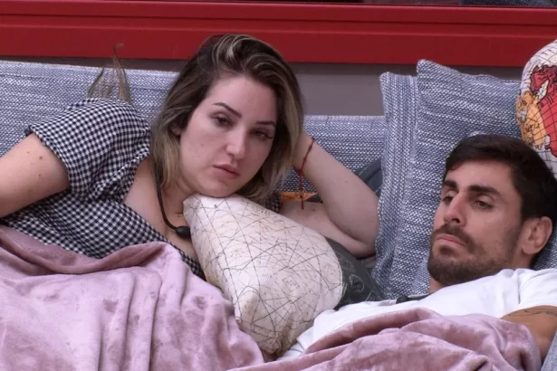 Amanda de cabelo solto, mão esquerda na cabeça, deitada ao lado de Cara de Sapato no sofá da sala do BBB 23