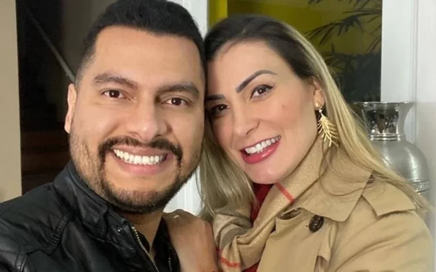 Thiago Lemos de camisa preta, sorrindo, ao lado de Andressa Urach de sobretudo marrom