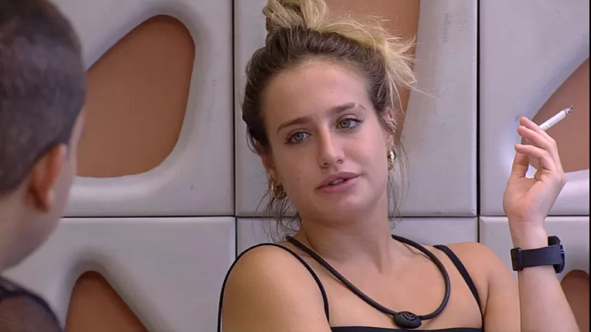 Bruna Griphao de regata preta, cabelo preso, segurando um cigarro, sentada na varada da casa do BBB 23