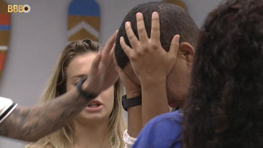 Bruno Gaga com a mão na cabeça, em pé, sendo acolhido por brothers na cozinha do BBB 23