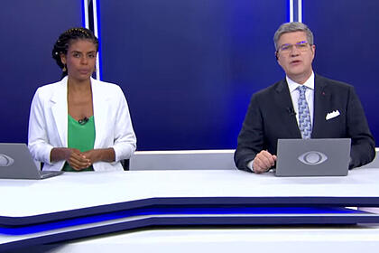 Cynthia Martins e Felipe Vieira sentados na bancada do Jornal da Noite