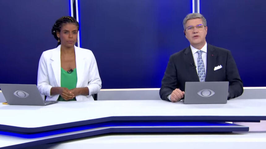 Cynthia Martins e Felipe Vieira sentados na bancada do Jornal da Noite