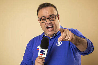 Everaldo Marques com um microfone da Globo em mãos e apontando o dedo para a câmera, em foto de divulgação e posada