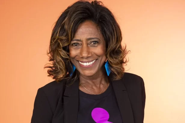 Gloria Maria de blazer e camisa preta com a logo do Criança Esperança durante ensaio fotográfico em studio com iluminação em tons de magenta