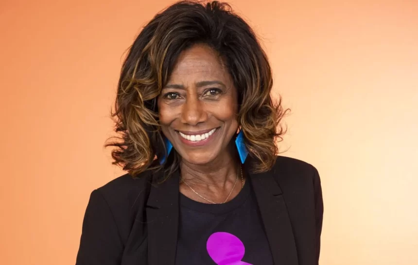 Gloria Maria de blazer e camisa preta com a logo do Criança Esperança durante ensaio fotográfico em studio com iluminação em tons de magenta