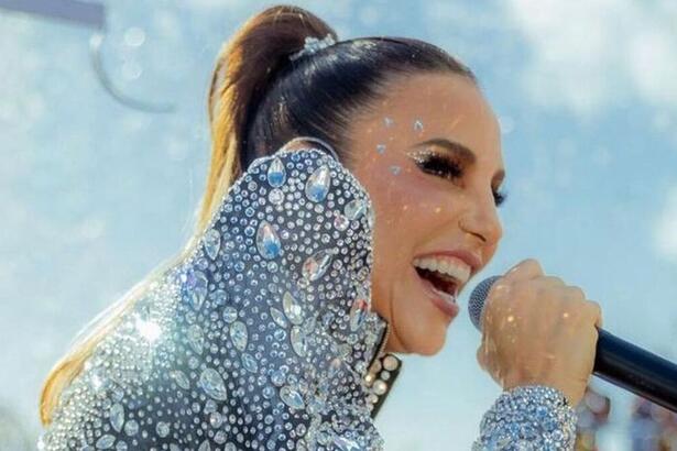 Ivete Sangalo segurando um microfone, com look prata brilhoso, durante carnaval de salvador