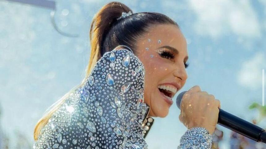 Ivete Sangalo segurando um microfone, com look prata brilhoso, durante carnaval de salvador