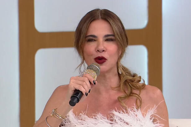 Luciana Gimenez com uma roupa branca, sentada no sofá do Superpop, da RedeTV!