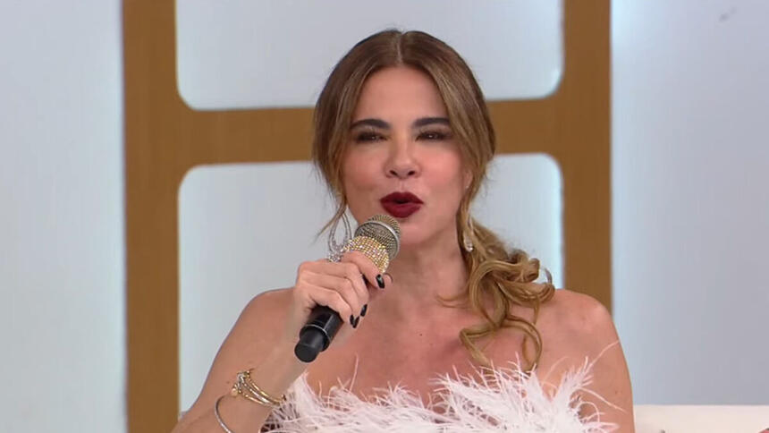 Luciana Gimenez com uma roupa branca, sentada no sofá do Superpop, da RedeTV!