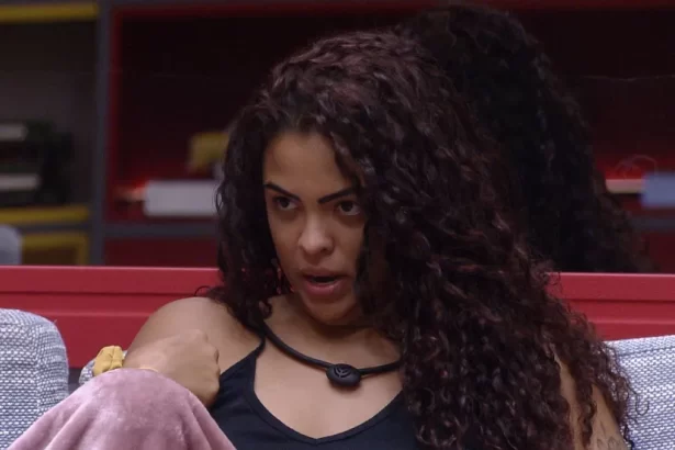 Paula Freitas de cabelo solto, camisa regata preta, microfone no pescoço, sentada no sofá da sala do BBB 23