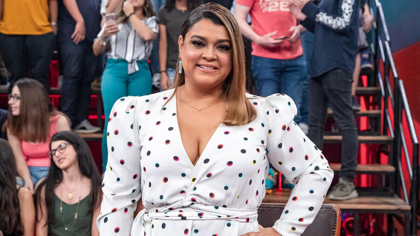 Preta Gil em foto posada, com as mãos na cintura, utilizando um vestido brando de bolinhas