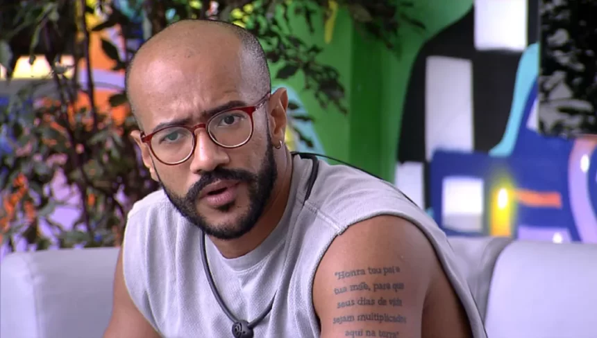 Ricardo de camisa regata cinza, de oculos de grau, sentado num banco branco, na varanda do BBB 23