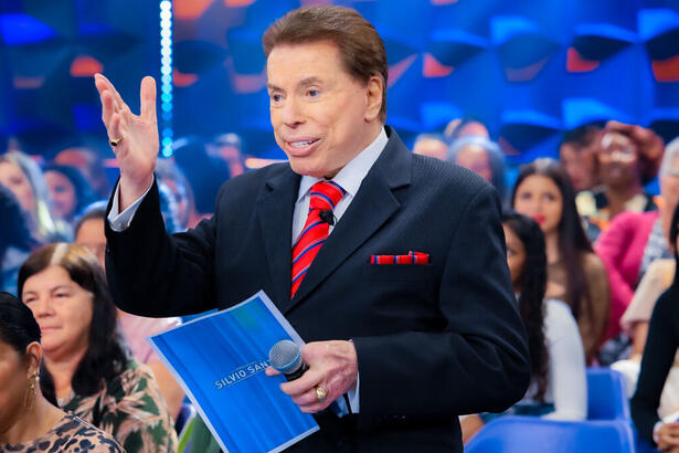 Silvio Santos com uma ficha nas suas mãos, em trecho do Programa Silvio Santos, em frente ao auditório