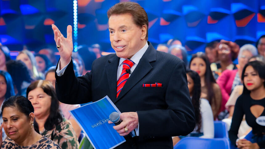 Silvio Santos com uma ficha nas suas mãos, em trecho do Programa Silvio Santos, em frente ao auditório