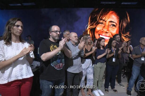 Jornalistas da TV Globo no Rio de Janeiro, no cenário do Jornal Nacional aplaudem Glória Maria, que apaece no telão.