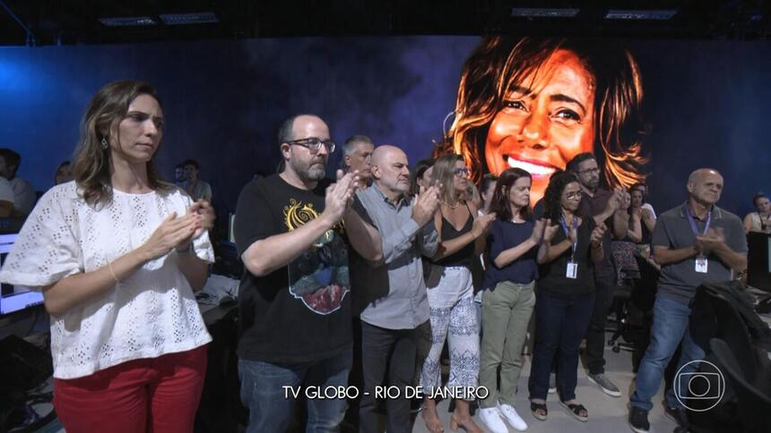 Jornalistas da TV Globo no Rio de Janeiro, no cenário do Jornal Nacional aplaudem Glória Maria, que apaece no telão.