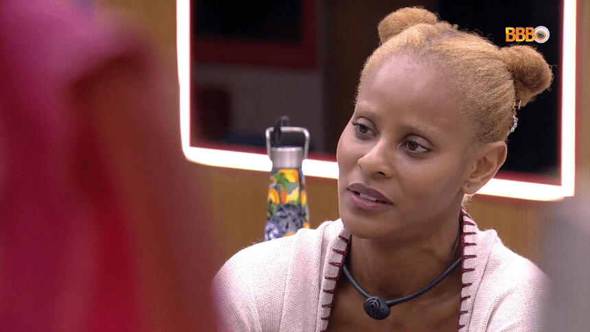 Aline Wirley de cabelo preso, camisa branca, sentada em um dos espaços da casa do BBB 23