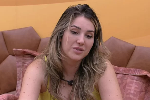 Amanda de regata amarela, cabelo solto, sentada na cama do Quarto Deserto do BBB 23