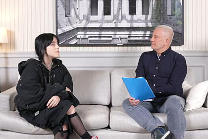 Billie Eilish em frente ao repórter Alberto Pereira Jr. sentados em um sofá, em trecho da entrevista para o Fantástico