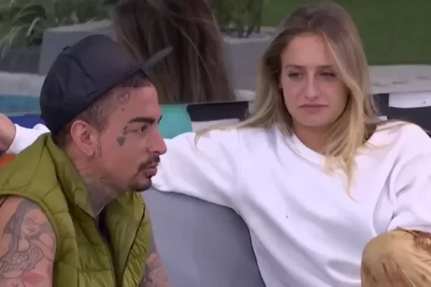 Bruna Griphao de cabelo solto, camisa branca, sentada num sofá ao lado de MC Guimê, de chapéu preto, camisa verde, com semblante sério