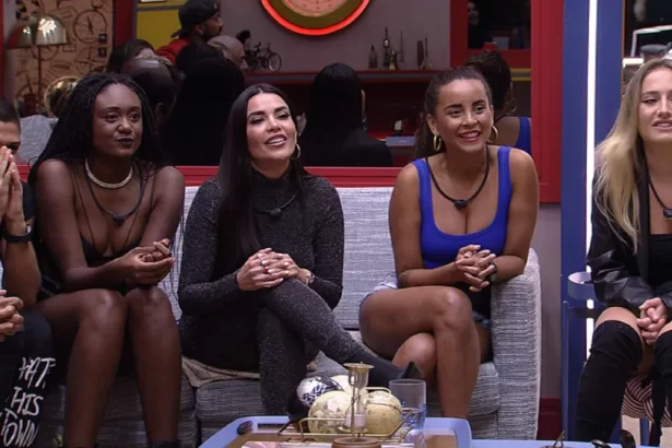 Dania sentada ao lado de Aline, Sarah e Bruna, no sofá, em frente ao telão da sala do BBB 23