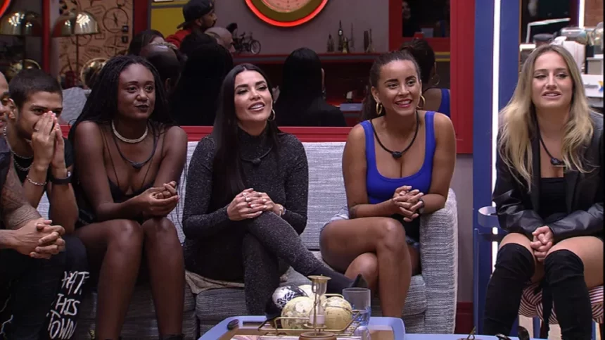 Dania sentada ao lado de Aline, Sarah e Bruna, no sofá, em frente ao telão da sala do BBB 23