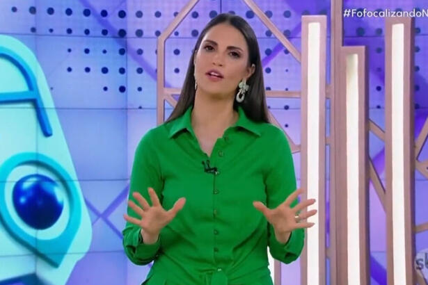 Chris Flores com um vestido verde, gesticulando com as mãos, em pé, no estúdio do Fofocalizando