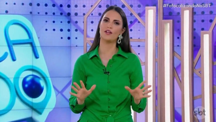 Chris Flores com um vestido verde, gesticulando com as mãos, em pé, no estúdio do Fofocalizando