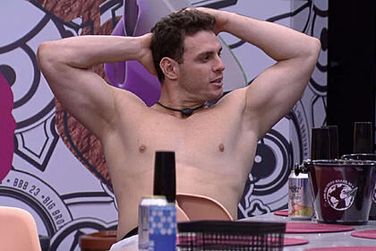 Gustavo sem camisa, com as mãos na cabeça, sentado na Casa do Reencontro no BBB 23