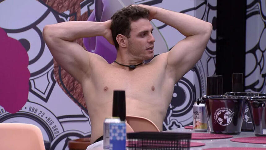 Gustavo sem camisa, com as mãos na cabeça, sentado na Casa do Reencontro no BBB 23