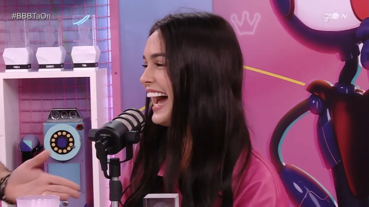 Larissa de camisa rosa, sorrindo, em frente a um microfone