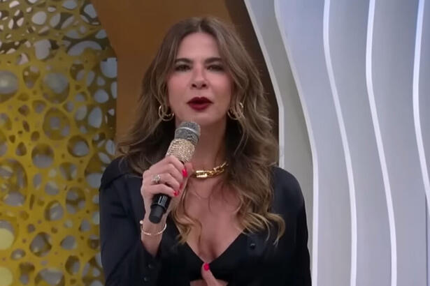 Luciana Gimenez, em pé, no estúdio do SuperPop, com um microfone em mãos