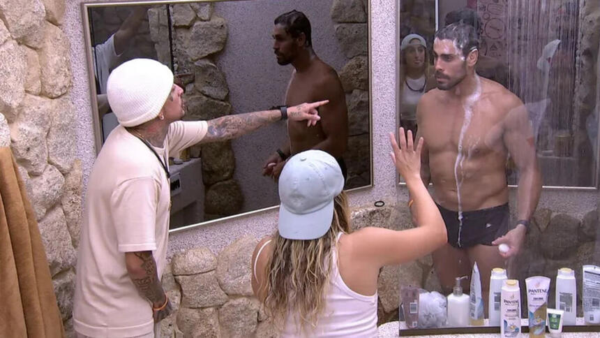 MC Guimê apontando para Cara de Sapato, que está tomando banho, durante discussão no banheiro do BBB 23. Bruna Griphao entre eles, tendo interferir e apaziguar