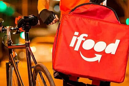 Um entregador de bicicleta ajeitando a mochila de entrada do iFood