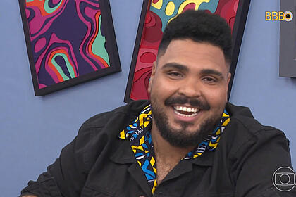 Paulo Vieira sorrindo de jaqueta preta e camisa social em tons de amarelo e ciano durante gravação do Big Terapia do BBB 23, da TV Globo
