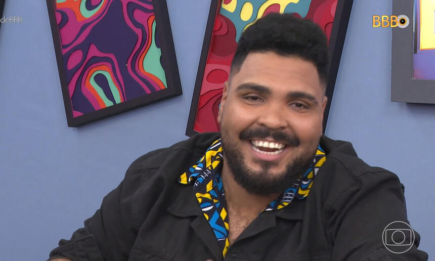 Paulo Vieira sorrindo de jaqueta preta e camisa social em tons de amarelo e ciano durante gravação do Big Terapia do BBB 23, da TV Globo